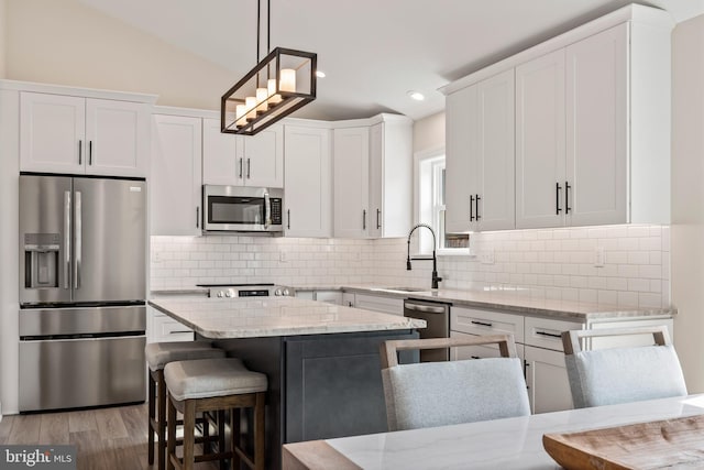 kitchen with decorative light fixtures, vaulted ceiling, light stone counters, appliances with stainless steel finishes, and white cabinets