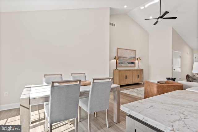 dining space with ceiling fan, high vaulted ceiling, visible vents, baseboards, and light wood-type flooring