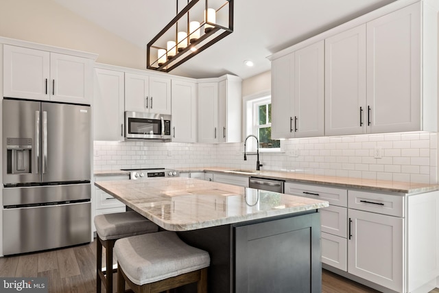 kitchen featuring vaulted ceiling, appliances with stainless steel finishes, a center island, hanging light fixtures, and white cabinetry