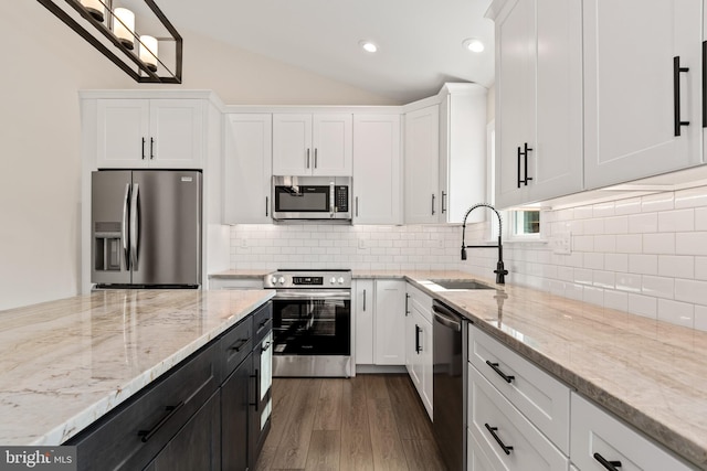 kitchen featuring stainless steel appliances, wood finished floors, a sink, white cabinetry, and vaulted ceiling