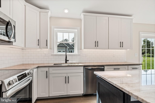 kitchen with white cabinets, hardwood / wood-style floors, appliances with stainless steel finishes, light stone counters, and sink