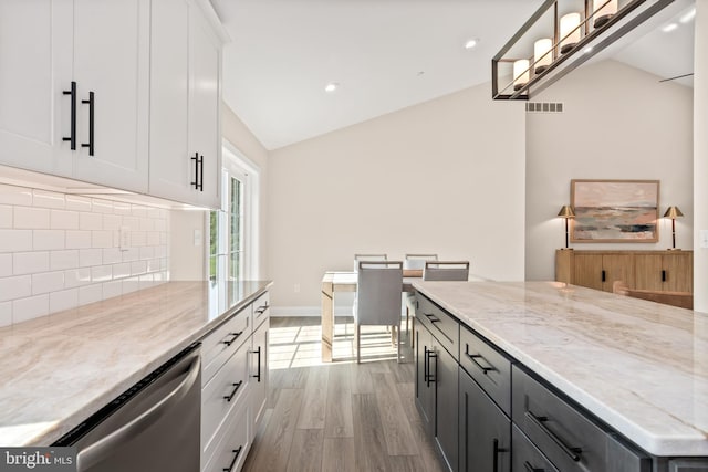 kitchen featuring dishwasher, light stone counters, vaulted ceiling, white cabinets, and light hardwood / wood-style floors