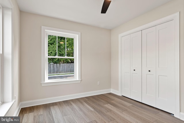 unfurnished bedroom featuring a ceiling fan, a closet, light wood-style flooring, and baseboards