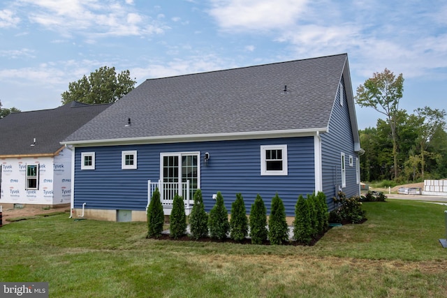 rear view of house with a lawn and roof with shingles