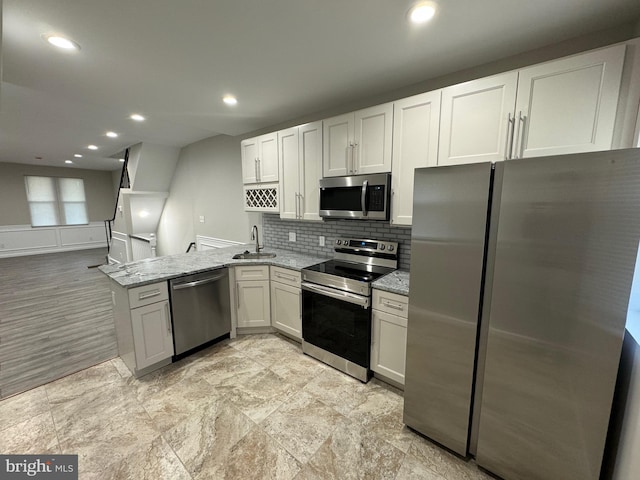 kitchen with stainless steel appliances, sink, kitchen peninsula, light stone countertops, and white cabinets