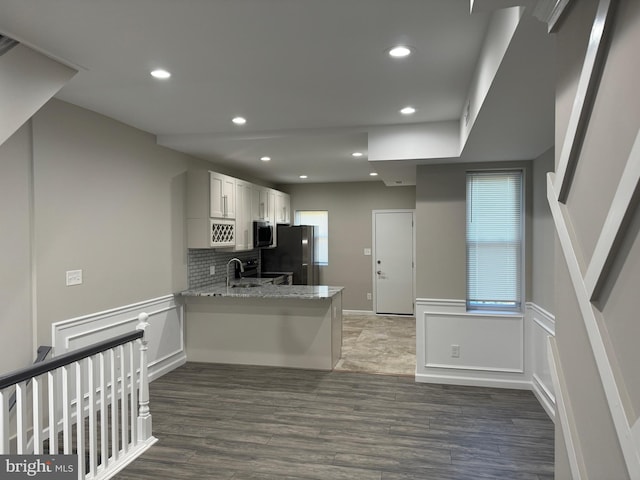 kitchen with stainless steel appliances, white cabinetry, kitchen peninsula, light stone countertops, and dark wood-type flooring