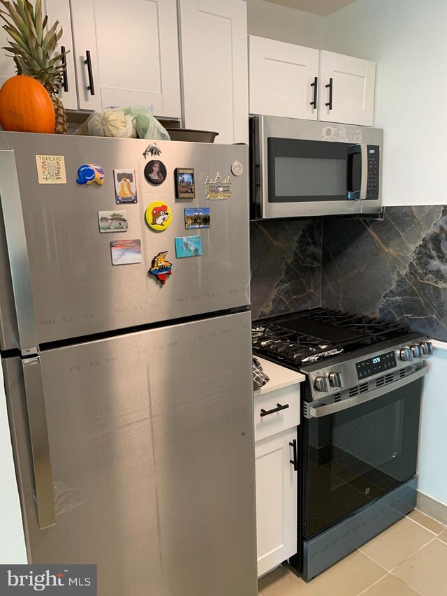 kitchen featuring hanging light fixtures, white range with gas cooktop, white cabinets, decorative backsplash, and light tile patterned floors