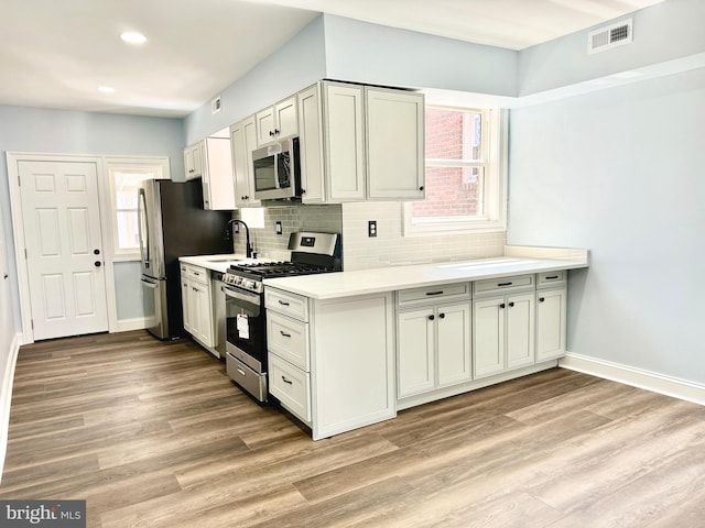 kitchen featuring decorative backsplash, white cabinets, appliances with stainless steel finishes, light wood-type flooring, and sink