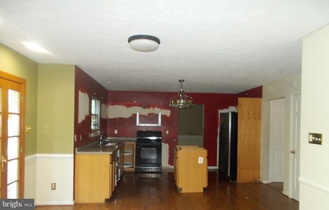 kitchen featuring a textured ceiling, black range oven, dark wood-type flooring, stainless steel refrigerator, and sink