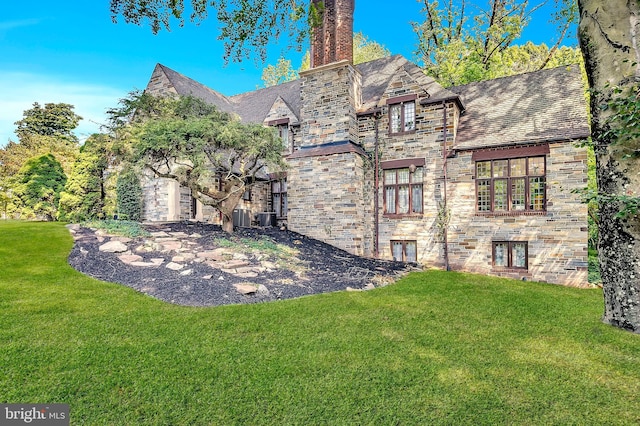 view of front of property featuring stone siding, a high end roof, central AC unit, and a front yard