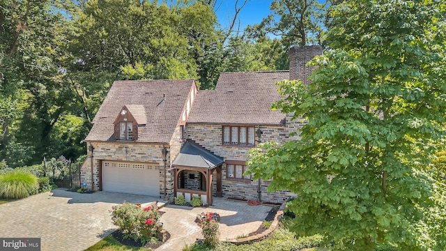 tudor-style house featuring decorative driveway, stone siding, and a garage