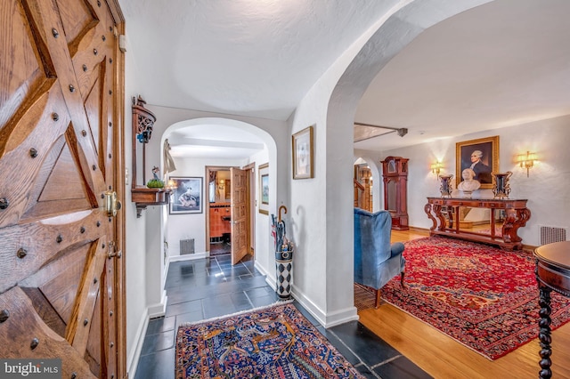 corridor featuring visible vents, arched walkways, and baseboards