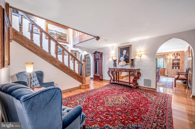 living room featuring arched walkways, wood finished floors, visible vents, baseboards, and stairway