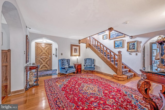 entryway with stairway, baseboards, arched walkways, and wood finished floors