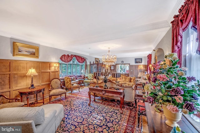 living room with crown molding, wood finished floors, a decorative wall, and an inviting chandelier