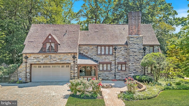 tudor home featuring a garage, stone siding, a chimney, decorative driveway, and a high end roof