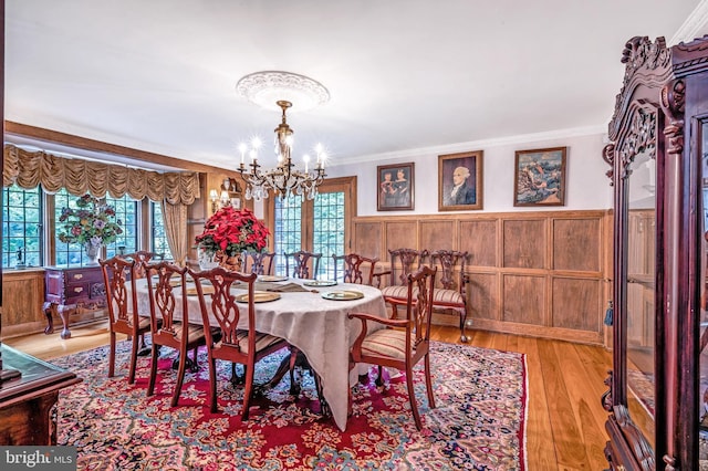 dining space with an inviting chandelier, light wood-style flooring, ornamental molding, and a wainscoted wall