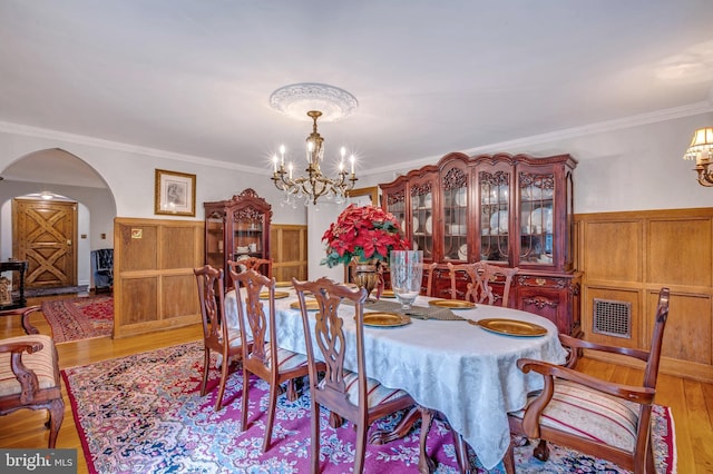 dining room featuring arched walkways, a notable chandelier, visible vents, ornamental molding, and light wood-type flooring