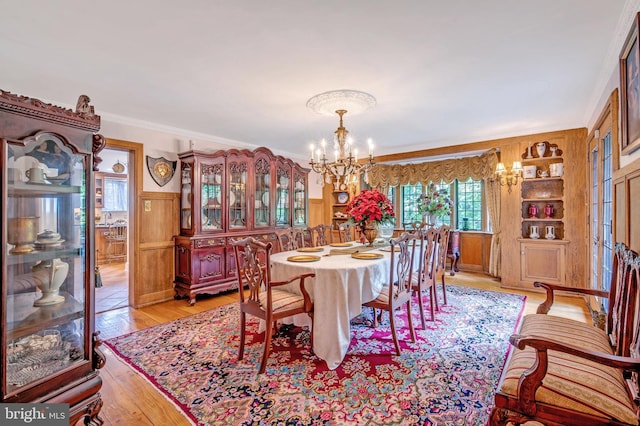 dining space featuring wainscoting, light wood-style flooring, ornamental molding, built in shelves, and a chandelier