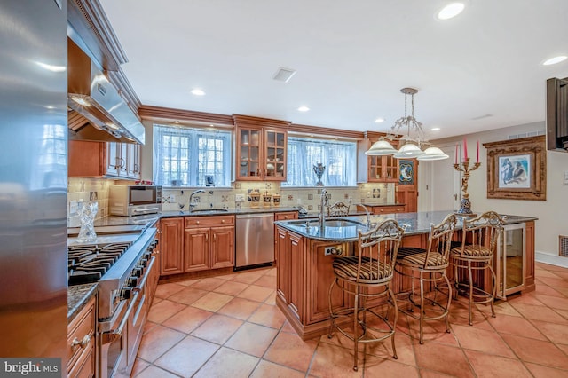 kitchen with a kitchen breakfast bar, appliances with stainless steel finishes, a center island with sink, decorative backsplash, and glass insert cabinets