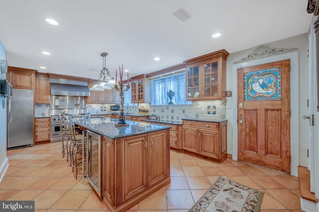 kitchen featuring a kitchen island, appliances with stainless steel finishes, brown cabinets, a kitchen breakfast bar, and wall chimney range hood