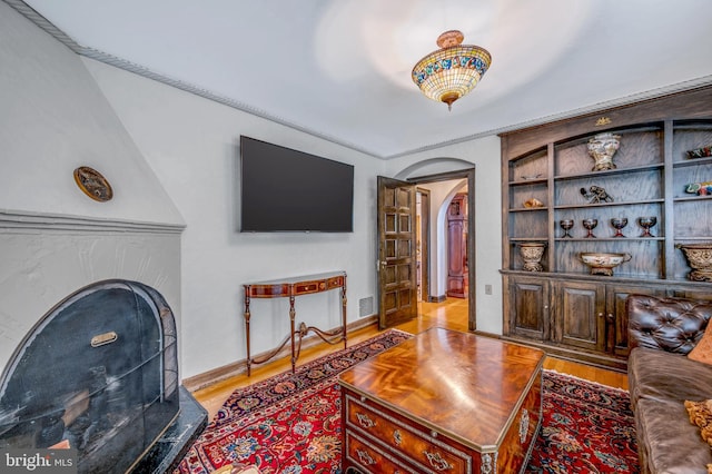 living room with visible vents, arched walkways, a fireplace with raised hearth, and wood finished floors