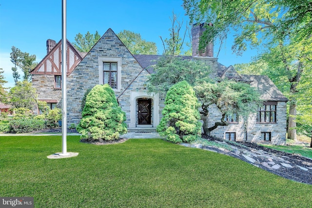 tudor home featuring stone siding, a chimney, and a front yard