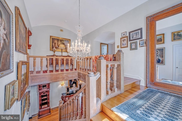 interior space featuring arched walkways, a notable chandelier, lofted ceiling, wood finished floors, and baseboards