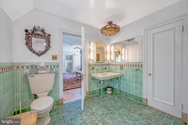 bathroom featuring a wainscoted wall, toilet, lofted ceiling, and tile walls