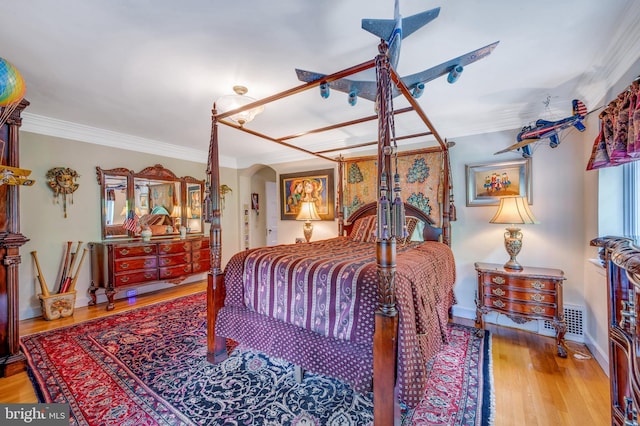 bedroom with baseboards, visible vents, arched walkways, wood finished floors, and crown molding