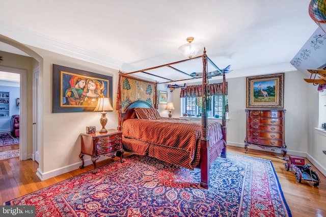 bedroom featuring baseboards, arched walkways, wood finished floors, and crown molding