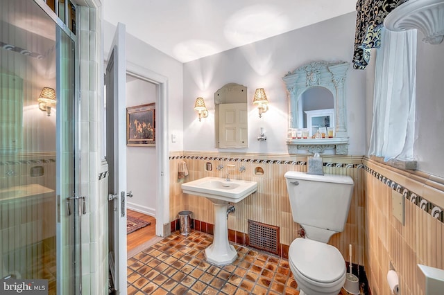 bathroom with visible vents, wainscoting, toilet, a shower stall, and tile walls