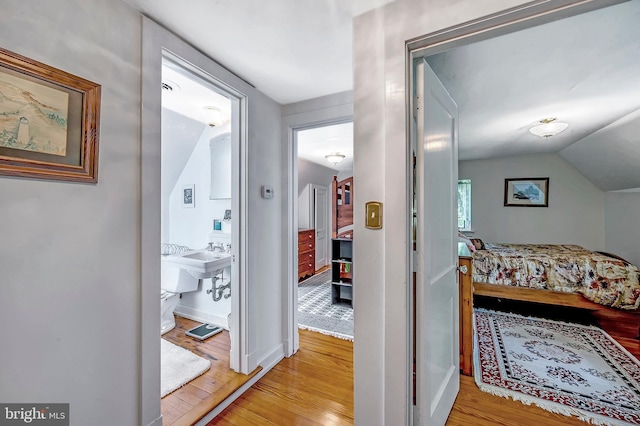 bedroom with light wood finished floors, ensuite bath, baseboards, and vaulted ceiling