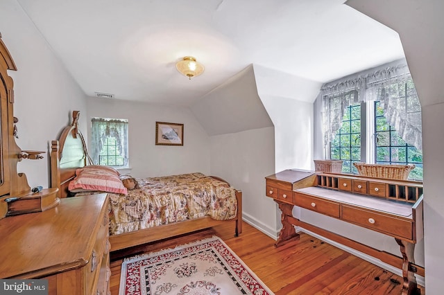 bedroom with lofted ceiling, visible vents, baseboards, and wood finished floors