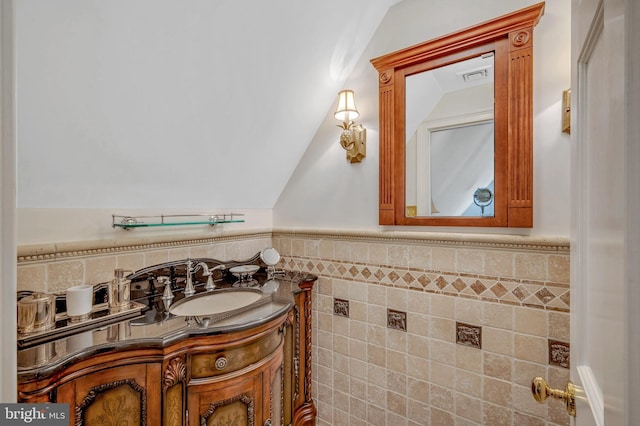 bathroom featuring visible vents, wainscoting, vaulted ceiling, vanity, and tile walls