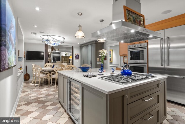 kitchen featuring a center island, decorative light fixtures, stainless steel appliances, beverage cooler, and island range hood