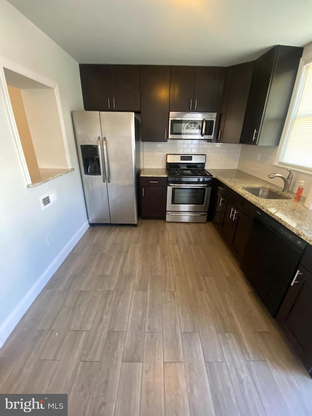 kitchen featuring a sink, appliances with stainless steel finishes, light wood-type flooring, light stone countertops, and tasteful backsplash