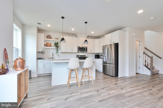 kitchen with appliances with stainless steel finishes, tasteful backsplash, a center island, white cabinetry, and light wood-type flooring