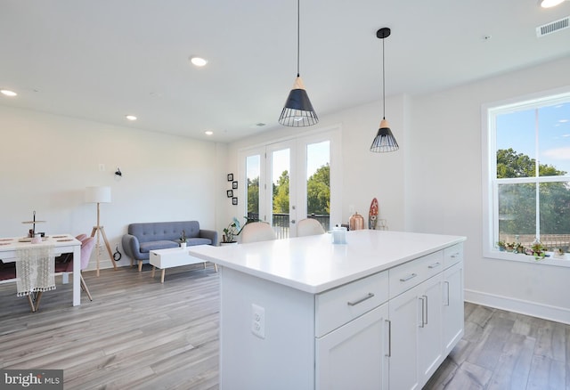 kitchen featuring light wood-type flooring, white cabinets, decorative light fixtures, and a healthy amount of sunlight