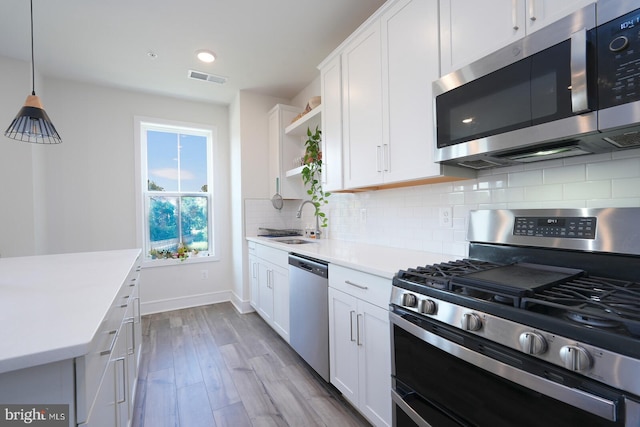 kitchen with appliances with stainless steel finishes, hanging light fixtures, sink, hardwood / wood-style flooring, and white cabinets