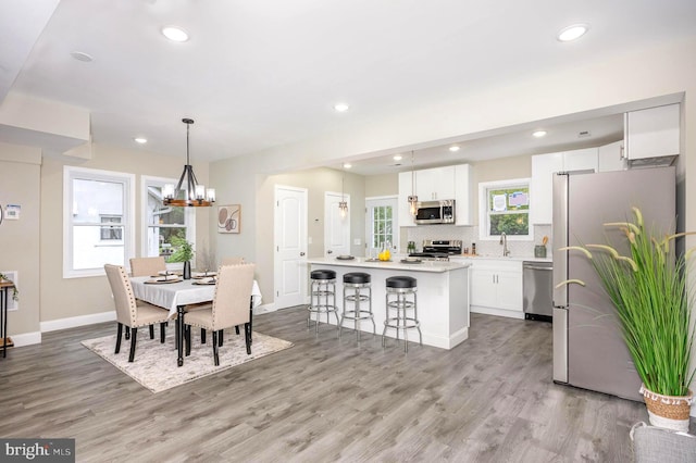 kitchen featuring stainless steel appliances, a center island, a kitchen bar, light wood-type flooring, and white cabinets