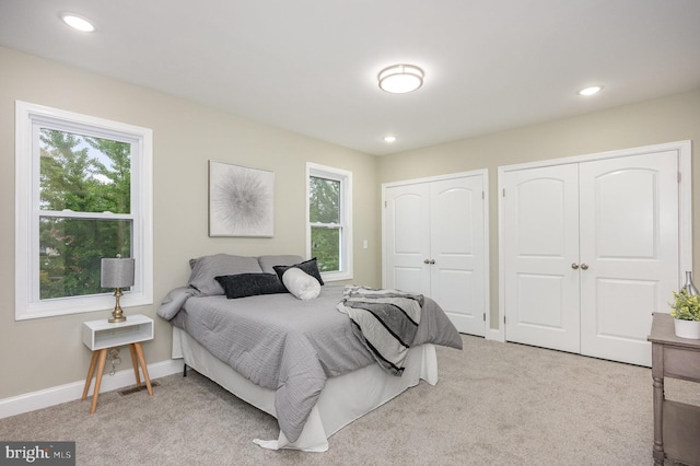 bedroom featuring light carpet, multiple windows, and two closets