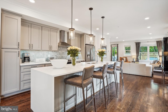 kitchen with dark hardwood / wood-style floors, wall chimney exhaust hood, a center island with sink, pendant lighting, and gray cabinets