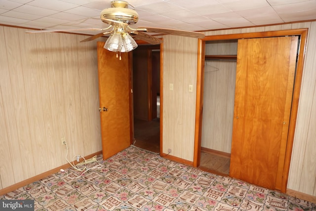 unfurnished bedroom with ceiling fan, wooden walls, a closet, and baseboards