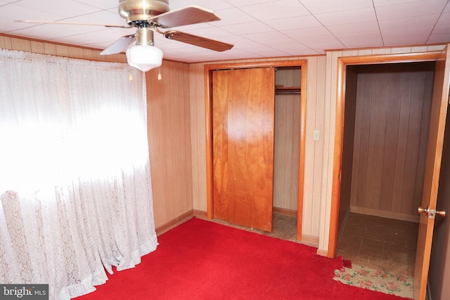 unfurnished bedroom with wooden walls, a ceiling fan, baseboards, a closet, and carpet