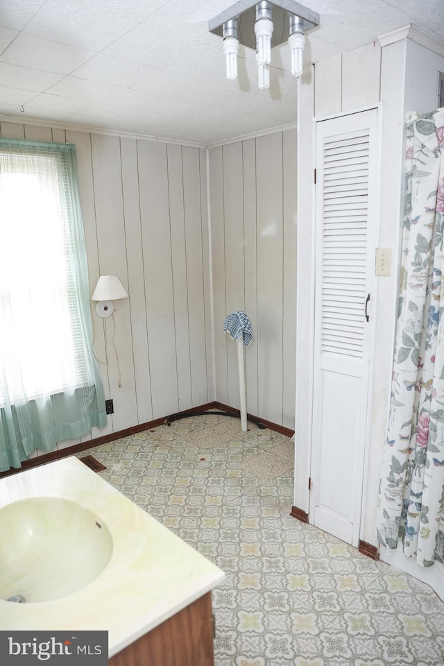 bathroom with wood walls, vanity, baseboards, and tile patterned floors