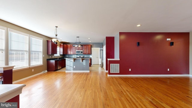 kitchen featuring light wood finished floors, stainless steel appliances, visible vents, open floor plan, and baseboards