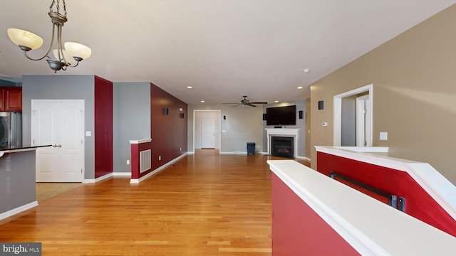 interior space with pendant lighting, a fireplace, visible vents, light wood-type flooring, and ceiling fan with notable chandelier