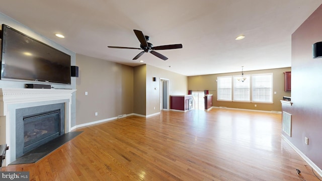 unfurnished living room featuring a ceiling fan, a fireplace with flush hearth, light wood-style flooring, and baseboards