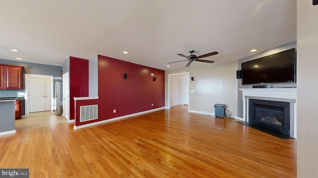 unfurnished living room featuring visible vents, light wood-style floors, a fireplace with flush hearth, ceiling fan, and baseboards